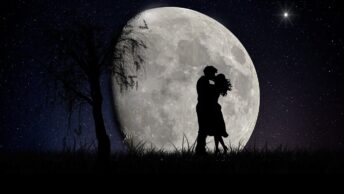A couple hugging at night and full moon behind.
