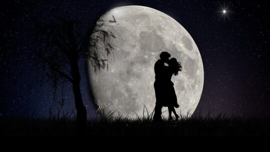 A couple hugging at night and full moon behind.